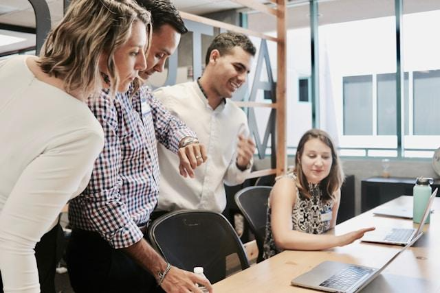Woman sitting at a table with her coworkers standing next to her